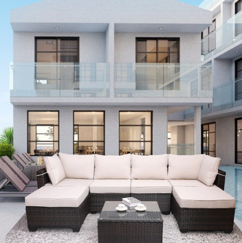 Outdoor patio furniture set including a sofa and a coffee table with cushions, placed on a balcony with a modern building in the background.
