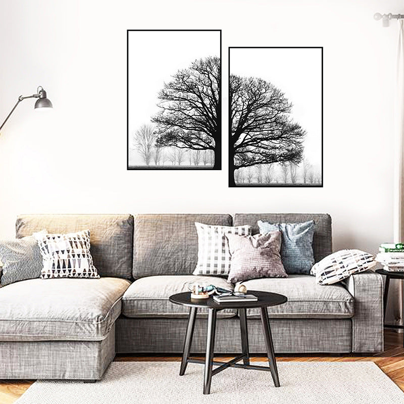 Two black and white tree paintings hanging on a wall above a grey sofa, with a small round table in front of the sofa displaying decorative items.