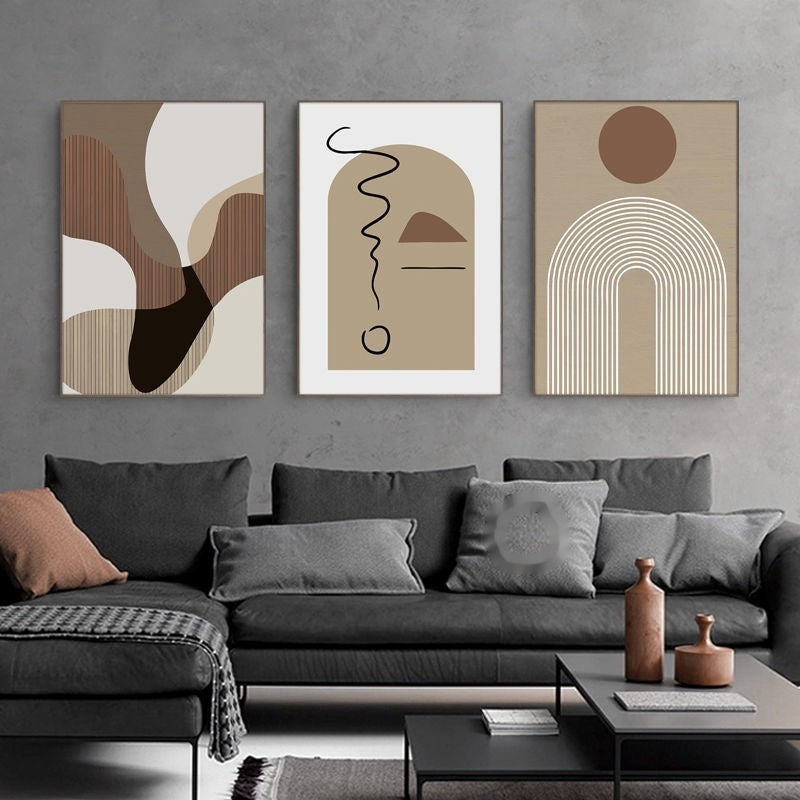 A set of three decorative wall paintings featuring abstract geometric designs, displayed above a modern gray sofa in a minimalist living room setting.